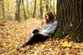 Young beautiful girl in a gray jacket sitting in the autumn forest near a large tree with a mobile phone Royalty Free Stock Photo