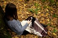 Young beautiful girl in a gray jacket sitting in the autumn forest near a large tree with a mobile phone Royalty Free Stock Photo