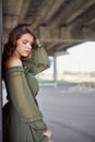 A young beautiful girl in a green dress poses under a concrete bridge, modern architecture