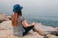 Young beautiful girl in a hat practicing yoga and meditating on stones next to the sea. Recreation. Vacation. Relaxation Royalty Free Stock Photo