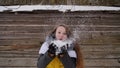 Young beautiful girl having fun blowing snow on the camera in winter clothes on the background of a wooden house in the Royalty Free Stock Photo