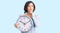 Young beautiful girl holding big clock serious face thinking about question with hand on chin, thoughtful about confusing idea Royalty Free Stock Photo