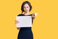 Young beautiful girl holding blank empty banner pointing with finger to the camera and to you, confident gesture looking serious Royalty Free Stock Photo