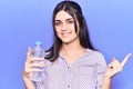 Young beautiful girl holding bottle of water smiling happy pointing with hand and finger to the side Royalty Free Stock Photo