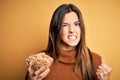 Young beautiful girl holding bowl of healthy cornflakes cereals over yellow background annoyed and frustrated shouting with anger,