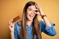 Young beautiful girl holding healthy protein bar standing over isolated yellow background with happy face smiling doing ok sign Royalty Free Stock Photo