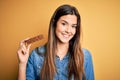 Young beautiful girl holding healthy protein bar standing over isolated yellow background with a happy face standing and smiling Royalty Free Stock Photo