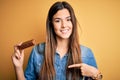 Young beautiful girl holding healthy protein bar standing over isolated yellow background with surprise face pointing finger to Royalty Free Stock Photo