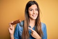 Young beautiful girl holding healthy protein bar standing over isolated yellow background very happy pointing with hand and finger Royalty Free Stock Photo