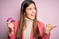 Young beautiful girl holding small car toy standing over isolated pink background pointing and showing with thumb up to the side Royalty Free Stock Photo