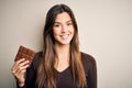 Young beautiful girl holding sweet bar of chocolate over isolated white background with a happy face standing and smiling with a Royalty Free Stock Photo