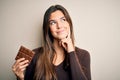 Young beautiful girl holding sweet bar of chocolate over isolated white background serious face thinking about question, very Royalty Free Stock Photo