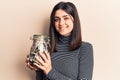 Young beautiful girl holding tips dollars jar looking positive and happy standing and smiling with a confident smile showing teeth