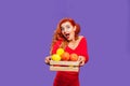 A young beautiful girl holds a basket of oranges and lemons. Red charismatic girl looks into the camera on a purple background.