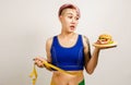 Young beautiful girl holds hamburger and measuring tape, on a light background