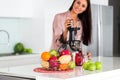 Young beautiful girl in the kitchen in the morning preparing fresh smoothies juice in a blender of their apple and tropical fruits Royalty Free Stock Photo