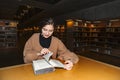 Girl in library turns page of book with smile Royalty Free Stock Photo