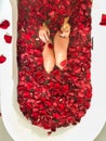 Top view of caucasian female in swimsuit sitting in bathtub with red petals. Royalty Free Stock Photo