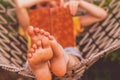 A young beautiful girl lies in a hammock and reads a book. Rest, summer vacation, leisure time concept. Selective focus on feets.