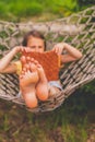 A young beautiful girl lies in a hammock and reads a book. Rest, summer vacation, leisure time concept. Selective focus on feets