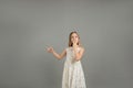 a young beautiful girl in a light dress points her finger to the side with a surprised face covering her mouth with her Royalty Free Stock Photo