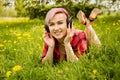 Young beautiful girl listening to music on headphones and lies on a green grass and dandelions Royalty Free Stock Photo