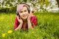 Young beautiful girl listening to music on headphones and lies on a green grass and dandelions Royalty Free Stock Photo