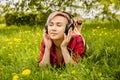 Young beautiful girl listening to music on headphones and lies on a green grass and dandelions Royalty Free Stock Photo