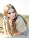 Young beautiful girl with long hair dressed in light short-sleeved dress leans her cheek on her fist and looks at camera Royalty Free Stock Photo