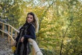 Young beautiful girl with long hair, in a fur jacket, stands on a wooden railing on a bright sunny day while walking in the autumn Royalty Free Stock Photo