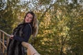 Young beautiful girl with long hair, in a fur jacket, stands on a wooden railing on a bright sunny day while walking in the autumn Royalty Free Stock Photo