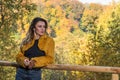 Young beautiful girl with long hair, in a fur jacket, stands on a wooden railing on a bright sunny day while walking in the autumn Royalty Free Stock Photo