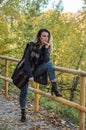 Young beautiful girl with long hair, in a fur jacket, stands on a wooden railing on a bright sunny day while walking in the autumn Royalty Free Stock Photo