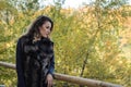 Young beautiful girl with long hair, in a fur jacket, stands on a wooden railing on a bright sunny day while walking in the autumn Royalty Free Stock Photo