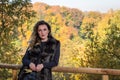 Young beautiful girl with long hair, in a fur jacket, stands on a wooden railing on a bright sunny day while walking in the autumn Royalty Free Stock Photo