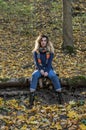 Young beautiful girl with long hair, with a scarf around his neck, sits on a log of fallen tree in the autumn forest among fallen Royalty Free Stock Photo