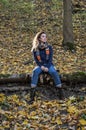 Young beautiful girl with long hair, with a scarf around his neck, sits on a log of fallen tree in the autumn forest among fallen Royalty Free Stock Photo