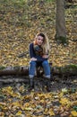 Young beautiful girl with long hair, with a scarf around his neck, sits on a log of fallen tree in the autumn forest among fallen Royalty Free Stock Photo