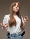 A young beautiful girl with long wavy rustic hair, nud makeup, wearing a white jersey, holds a makeup brush and blush