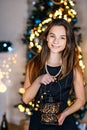 A young beautiful girl with a luminous candlestick in her hands near the New Year tree smiles joyfully. Merry Christmas