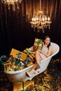 A young and beautiful girl is lying in the bath with New Year's gifts in golden wrappers o Royalty Free Stock Photo