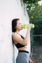 A young beautiful girl near a white wall in sportswear drinks water from a bottle. in the summer time Royalty Free Stock Photo