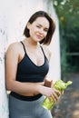 A young beautiful girl near a white wall in sportswear drinks water from a bottle. in the summer time Royalty Free Stock Photo