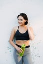 A young beautiful girl near a white wall in sportswear drinks water from a bottle. in the summer time Royalty Free Stock Photo