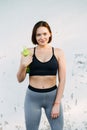 A young beautiful girl near a white wall in sportswear drinks water from a bottle. in the summer time Royalty Free Stock Photo