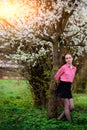 Young beautiful girl in a pink shirt standing under blossoming apple tree and enjoying a sunny day. Royalty Free Stock Photo
