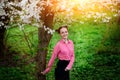 Young beautiful girl in a pink shirt standing under blossoming apple tree and enjoying a sunny day.