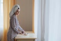 a young beautiful girl with hair wrapped in a towel and in pajamas puts a cup of tea or coffee on the table with a piece Royalty Free Stock Photo