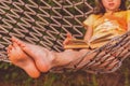 A young beautiful girl reads a book outdoors in a hammock. Summer vacation, leisure time concept. Selective focus on feets