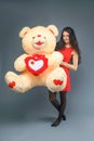 Young beautiful girl in red dress with big teddy bear soft toy happy smiling and playing on grey background Royalty Free Stock Photo